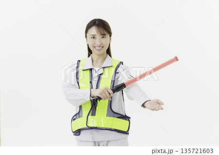 白背景の作業服の安全ベルトをつけて誘導灯を持つ若い日本人女性 白背景の作業服の安全ベルトをつけて誘導灯を持つ若い日本人女性 135721603