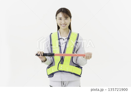 白背景の作業服の安全ベルトをつけて誘導灯を持つ若い日本人女性 白背景の作業服の安全ベルトをつけて誘導灯を持つ若い日本人女性 135721900