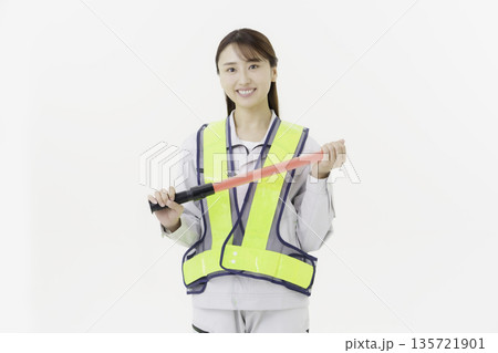 白背景の作業服の安全ベルトをつけて誘導灯を持つ若い日本人女性 白背景の作業服の安全ベルトをつけて誘導灯を持つ若い日本人女性 135721901