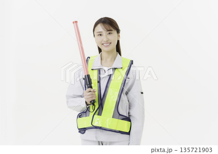 白背景の作業服の安全ベルトをつけて誘導灯を持つ若い日本人女性 白背景の作業服の安全ベルトをつけて誘導灯を持つ若い日本人女性 135721903