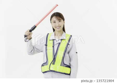 白背景の作業服の安全ベルトをつけて誘導灯を持つ若い日本人女性 白背景の作業服の安全ベルトをつけて誘導灯を持つ若い日本人女性 135721904