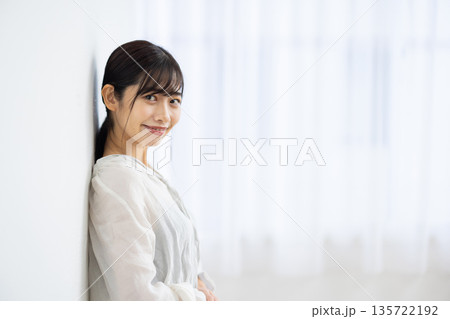 白い壁にもたれながら微笑む若い女性 135722192