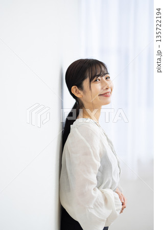 白い壁にもたれながら微笑む若い女性 135722194