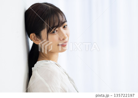 白い壁にもたれながら微笑む若い女性 135722197