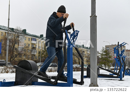 Man exercises outdoors on gym equipment in winter in a city park Man exercises outdoors on gym equipment in winter in a city park 135722622