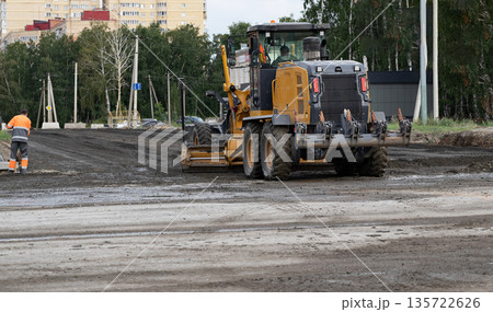 Construction machinery operates on a road at a work site in an urban area during daylight hours 135722626