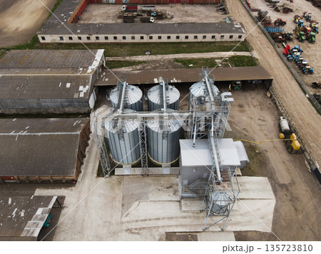 Drone view of grain elevator complex with silos, conveyors, warehouses and farm machinery parking area in countryside 135723810