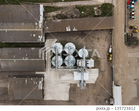 Drone overhead of grain storage plant with round metal silos and conveyor lines beside farm warehouses and service yard Drone overhead of grain storage plant with round metal silos and conveyor lines beside farm warehouses and service yard 135723812