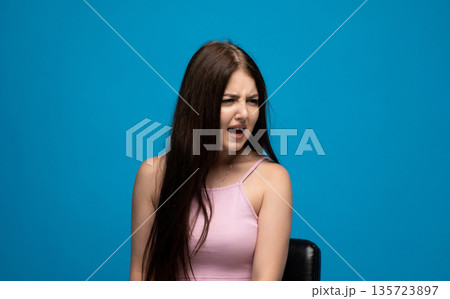 Young woman with confused facial expression looking aside against blue background, human emotions and reaction concept Young woman with confused facial expression looking aside against blue background, human emotions and reaction concept 135723897