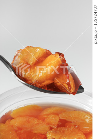 Fruit jelly with mandarin pieces in a metal spoon. Appetizing dessert close-up. 135724737