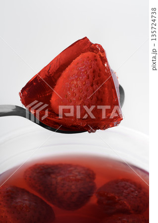 Fruit jelly with strawberry pieces in a metal spoon. Appetizing dessert close-up. Fruit jelly with strawberry pieces in a metal spoon. Appetizing dessert close-up. 135724738