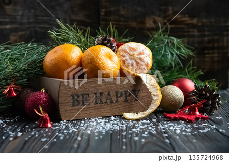 Orange mandarins in wooden box with fir apple, red balls, snowflakes on green fir branch background. Christmas card. Happy new year and merry christmas. High quality photo Orange mandarins in wooden box with fir apple, red balls, snowflakes on green fir branch background. Christmas card. Happy new year and merry christmas. High quality photo 135724968