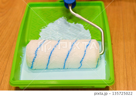 Paint roller is being dipped into a tray of blue paint, ready to be used for a home renovation project 135725022