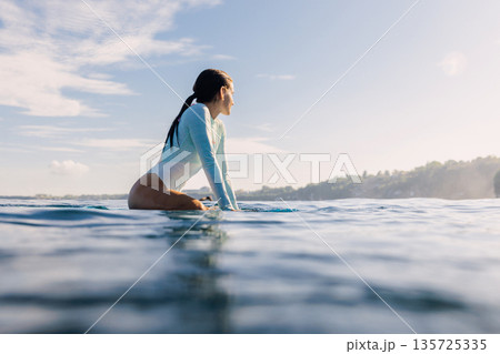 Beauty surf girl sitting on surfboard in ocean. Surfer woman in water Beauty surf girl sitting on surfboard in ocean. Surfer woman in water 135725335