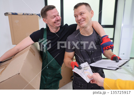 Two cheerful movers celebrate a successful job while exchanging payment in a bright, modern living space Two cheerful movers celebrate a successful job while exchanging payment in a bright, modern living space 135725917