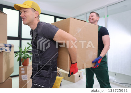 Friends joyfully moving boxes in a bright office space during a sunny afternoon 135725951