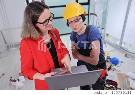 Collaborative planning session between a businesswoman and construction worker indoors Collaborative planning session between a businesswoman and construction worker indoors 135726131