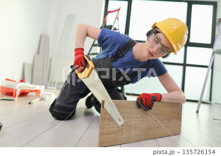 Skilled worker measures wooden plank while kneeling on floor in bright, modern workspace 135726154