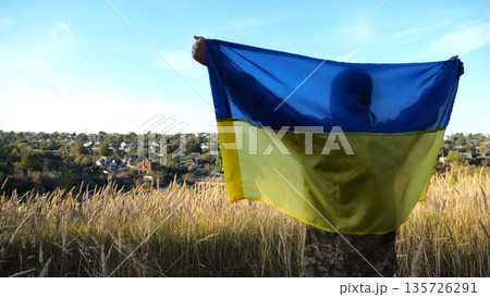 Military man in uniform stands with raised over head flag of Ukraine at countryside. Male ukrainian army soldier with lifted national banner in honor of victory against russian aggression. End of war Military man in uniform stands with raised over head flag of Ukraine at countryside. Male ukrainian army soldier with lifted national banner in honor of victory against russian aggression. End of war 135726291
