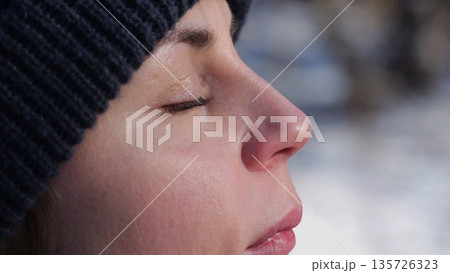 Detail view of attractive female face illuminating by warm rays of sun at winter day. Calm facial expression of young woman. Tranquil sight with green eyes of beautiful girl. Close up Detail view of attractive female face illuminating by warm rays of sun at winter day. Calm facial expression of young woman. Tranquil sight with green eyes of beautiful girl. Close up 135726323