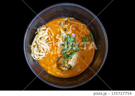 Northern Thai Khao Soi Chicken Curry Noodles in black bowl on black background. Northern Thai Khao Soi Chicken Curry Noodles in black bowl on black background. 135727754
