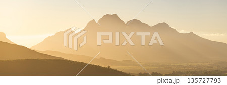 Golden morning mist obscures mountain peaks. Serene nature landscape with soft light. Atmospheric view for travel and outdoor design. 135727793