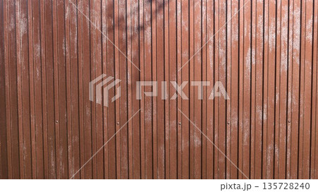 Brown metal fence with vertical convex lines in the structure, full frame, drops of moisture on street metal covering, condensation on dark iron sheet 135728240