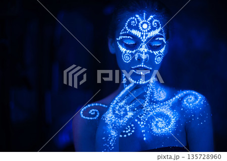 Body art on the body and hand of a girl glowing in the ultraviolet light. 135728960