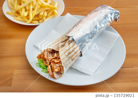 Delicious chicken kebab roll served on a white plate with crispy fries, showcasing vibrant colors and appetizing textures for food lovers 135729021