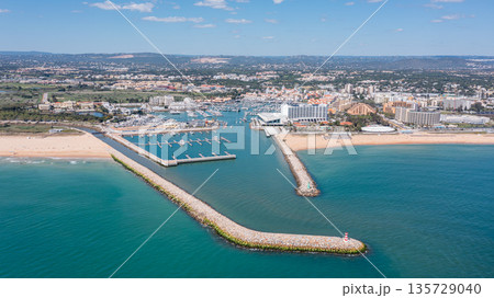People participate in activities at Vilamoura marina in Algarve, Portugal, with boats docked and a vibrant waterfront visible under a sunny sky. Aerial 135729040