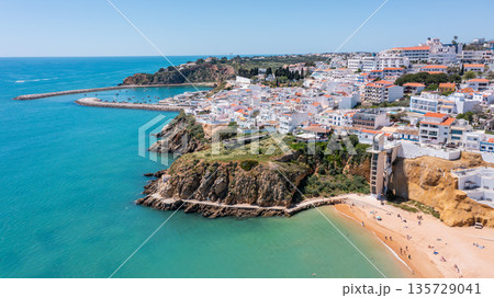 People relax on the beach and explore the marina in Albufeira, Portugal, as boats move in the water under a clear sky in summer time People relax on the beach and explore the marina in Albufeira, Portugal, as boats move in the water under a clear sky in summer time 135729041