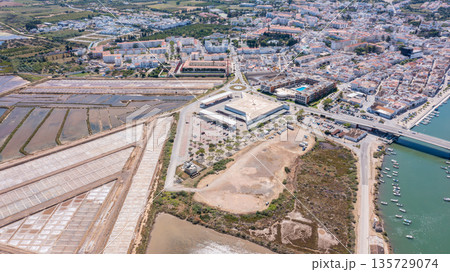 Tavira in Algarve with buildings, salt flats, a river, and parts of the ocean visible in the distance under sunny weather 135729074
