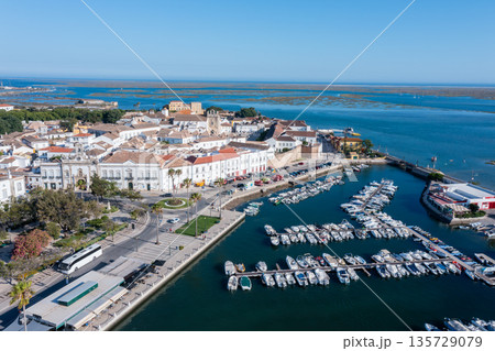 Visitors explore the dock in Faro, Algarve under clear skies. Boats are lined up in the water near the historic old town and Ria Formosa area Visitors explore the dock in Faro, Algarve under clear skies. Boats are lined up in the water near the historic old town and Ria Formosa area 135729079