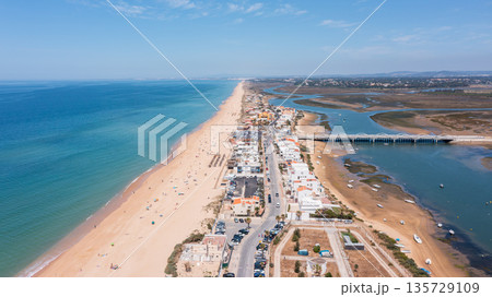Aerial view shows Praia de Faro with its long sandy beach and the nearby Ria Formosa. People enjoy the beach while boats rest in the water Aerial view shows Praia de Faro with its long sandy beach and the nearby Ria Formosa. People enjoy the beach while boats rest in the water 135729109