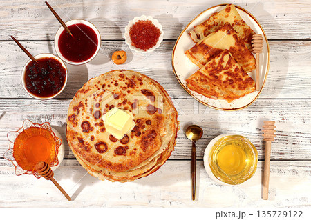 Delicious Russian pancakes with soft cheese, honey, jam, and sour cream on an elegant kitchen table. Maslenitsa concept and traditional Russian cuisine. Advertising banner for a cafe or restaurant. 135729122