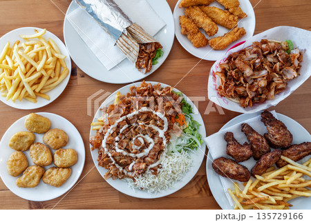 Delicious assortment of fast food including chicken, fries, and wraps arranged on wooden table, showcasing vibrant colors and tempting textures Delicious assortment of fast food including chicken, fries, and wraps arranged on wooden table, showcasing vibrant colors and tempting textures 135729166