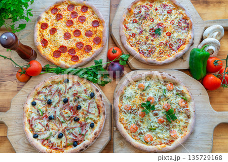 Assorted gourmet pizzas with various toppings displayed on wooden boards, showcasing vibrant colors and fresh ingredients for culinary delight Assorted gourmet pizzas with various toppings displayed on wooden boards, showcasing vibrant colors and fresh ingredients for culinary delight 135729168