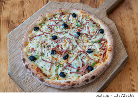 Delicious pizza topped with ham, olives, and green peppers on a wooden board, showcasing a mouthwatering culinary delight for food lovers 135729169