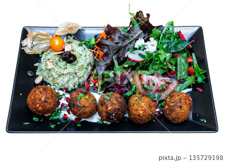 Colorful vegan Moroccan tabbouleh served on a black plate, featuring fresh greens, herbs, and flavorful falafel balls, perfect for healthy dining 135729198