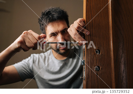 Portrait of professional technician male fixing door lock with screwdriver, performing installation and repair work on mechanism to ensure security and functionality within house. 135729352