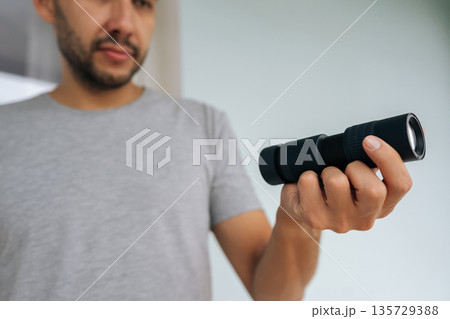 Close-up cropped shot of man person holding black monocular in hand, extending forward, focusing with optical instrument to observe something unseen. Concept of discovering, exploring, vision. Close-up cropped shot of man person holding black monocular in hand, extending forward, focusing with optical instrument to observe something unseen. Concept of discovering, exploring, vision. 135729388
