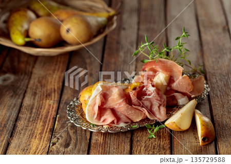 Prosciutto with pears and thyme on a silver tray. 135729588