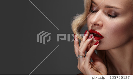 Sexy woman with striking fashion makeup, featuring bright red lips and red nails. Blond curly hairstyle completes glamorous look. Perfect pin-up beauty with bold style 135730127