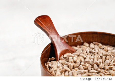 Peeled sunflower seeds in small wooden cup with little scoop, placed on white stone like board, closeup detail 135730238