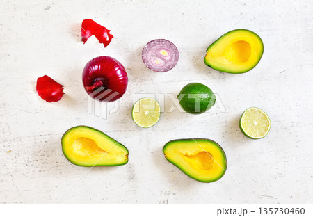 Avocado halves, limes and onions - basic guacamole ingredients on white working board, flat lay photo 135730460