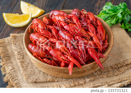 Wooden bowl of bright red boiled crawfish with lemon and parsley, rustic table 135731321