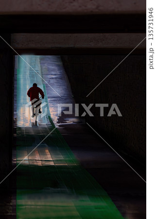 雨の日のアンダーパスを自転車で駆け抜ける男性 135731946