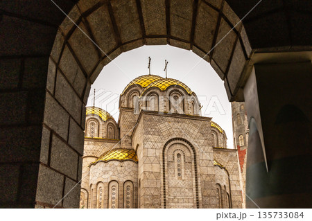 Holy Equal-to-the-Apostles Emperor Constantine and Empress Elena Orthodox church with golden domes framed by stone arch in Skopje, North Macedonia 135733084