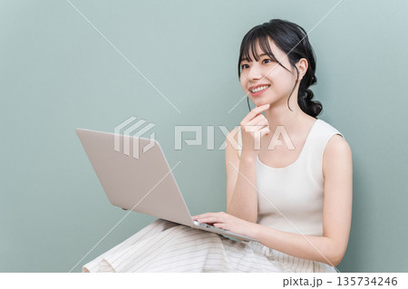 家でパソコンを使って笑顔で考える若いアジア人女性（楽しい,想像,構想,計画,プラン） 135734246