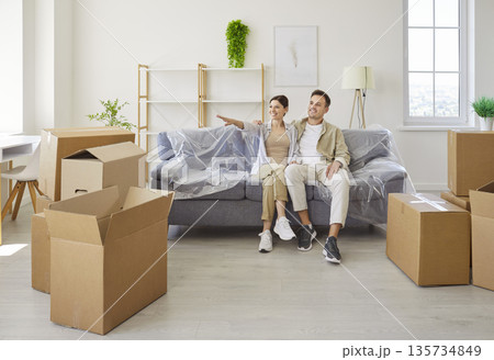 Smiling couple planning new apartment layout while sitting on sofa amid boxes Smiling couple planning new apartment layout while sitting on sofa amid boxes 135734849